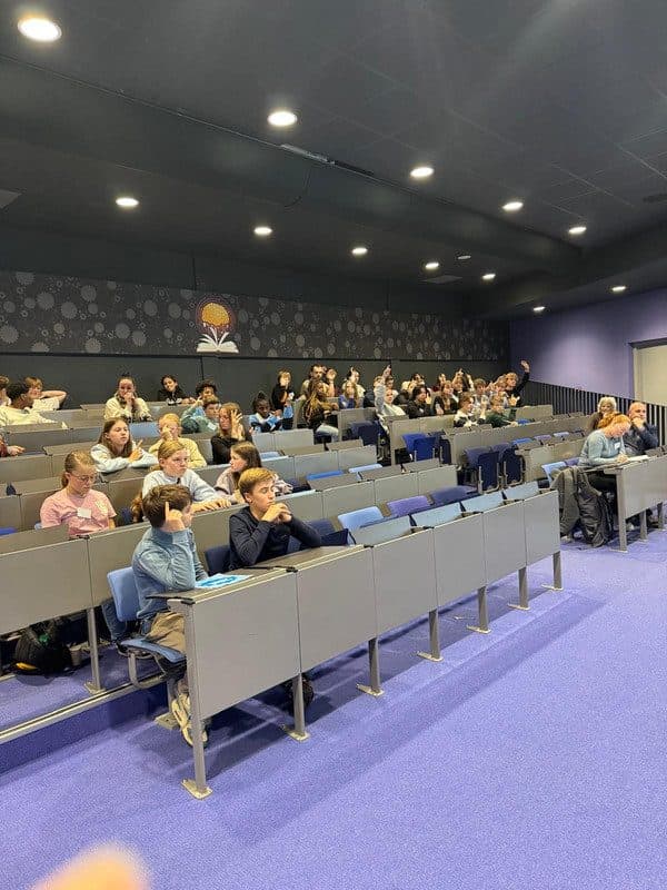 Leerlingen in een collegezaal tijdens een congres, met opgestoken handen